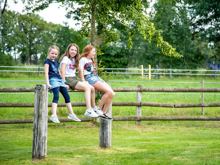 Familienhotel Landhus Laurenz im Münsterland: 3 Mädchen sitzen auf Zaun und lachen