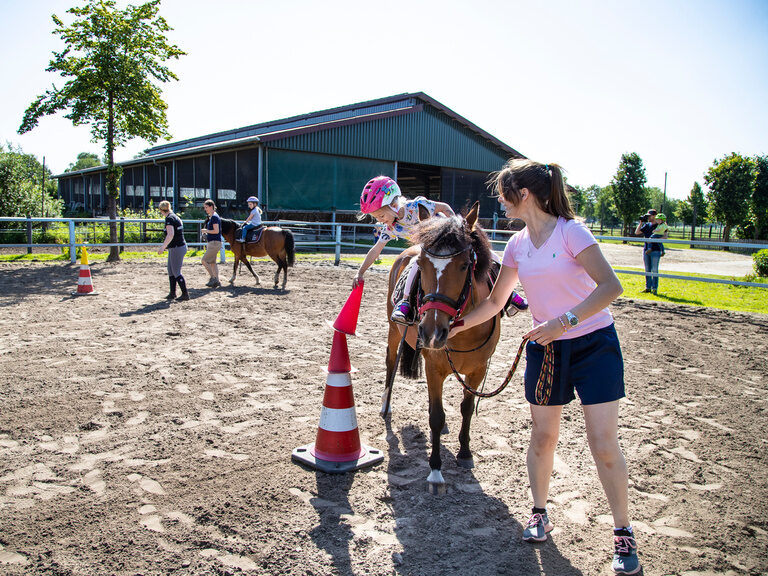 Familienhotel Landhus Laurenz im Münsterland: kleines Mädchen mit Pony am Reitplatz und wird von Betreuerin geführt