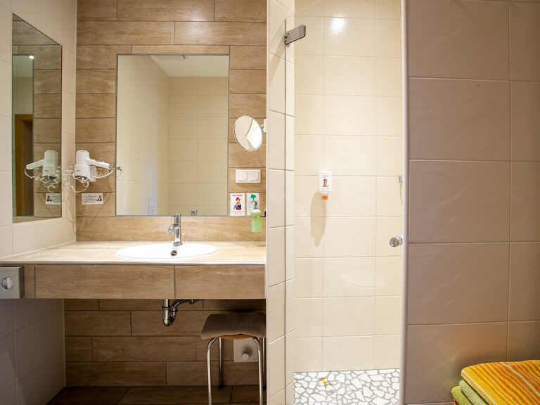 Familienhotel Landhus Laurenz im Münsterland: Badezimmer mit hellen Fliesen, Waschtisch, Spiegeln, Föhn, begehbarer Dusche, weißem Handtuchhalter