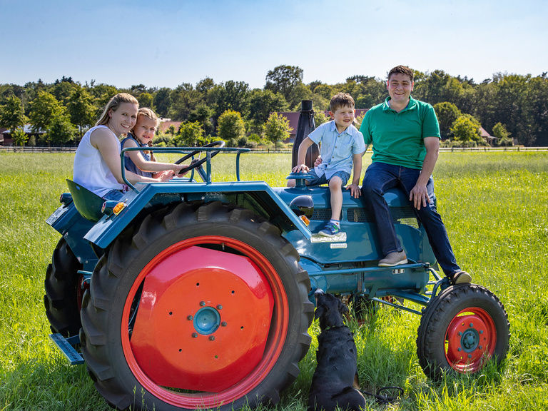 Familienhotel Landhus Laurenz im Münsterland: Familienfoto der Familie Laurenz, Inhaber des Hotels auf blauem Traktor