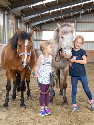 Kinder mit Pferden in Reithalle