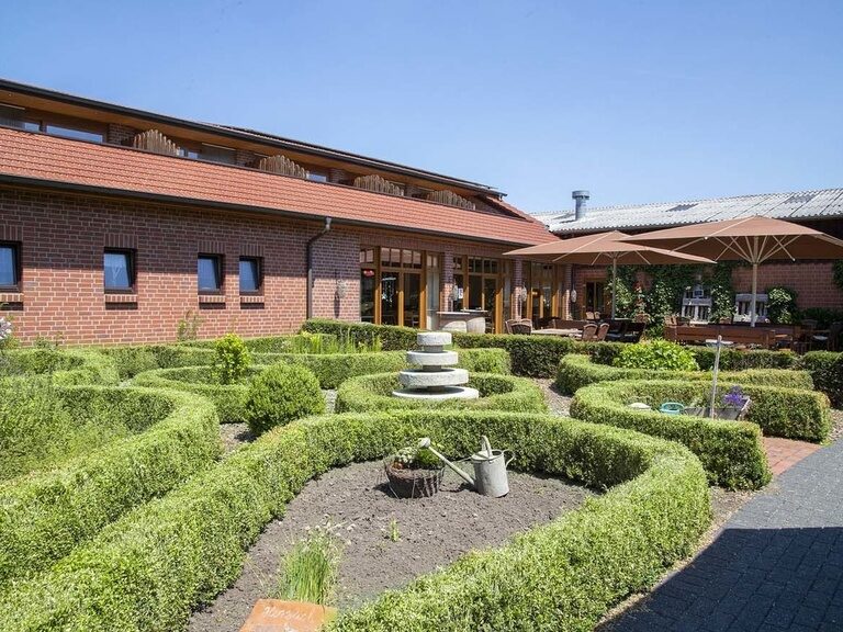 Familienhotel Landhus Laurenz im Münsterland: Hotel Außenansicht mit niedrigen Heckenfeldern bei schönem Wetter