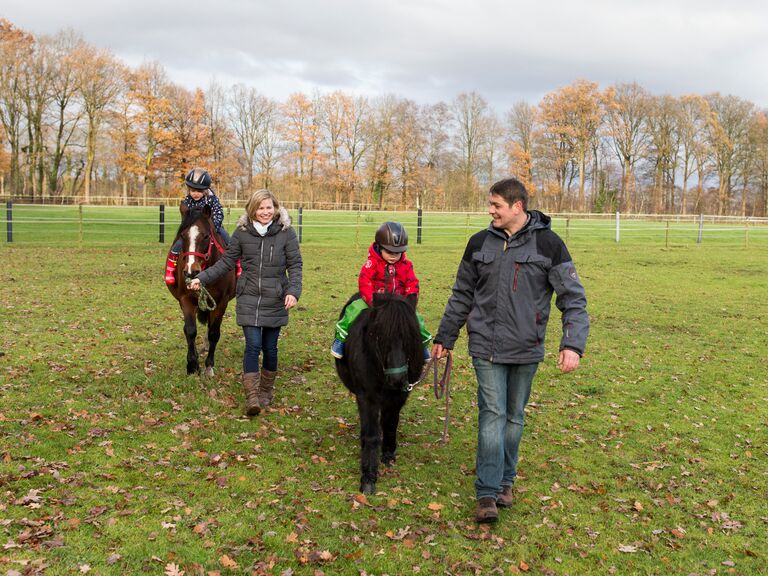 Familienhotel Landhus Laurenz im Münsterland: 2 Kinder beim Ponyreiten, werden von Mama und Papa über die Wiese geführt