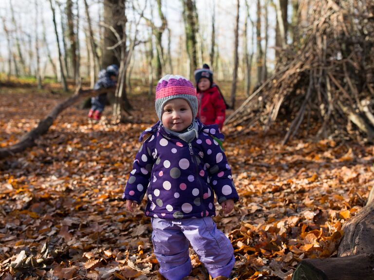 Familienhotel Landhus Laurenz im Münsterland: drei Kinder spielen im Herbstwald im Laub, kleines Mädchen lächelt in Winterkleidung in die Kamera