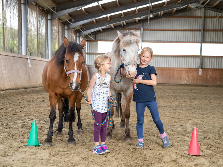 Familienhotel Landhus Laurenz im Münsterland: zwei Kinder mit zwei Pferden in Reithalle